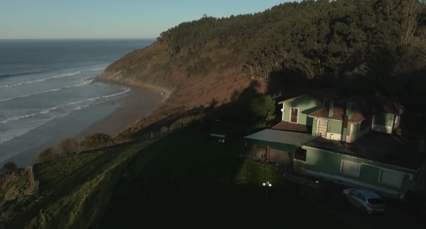 The house: green, on the hillside above the beach, with the sea and the waves on the left