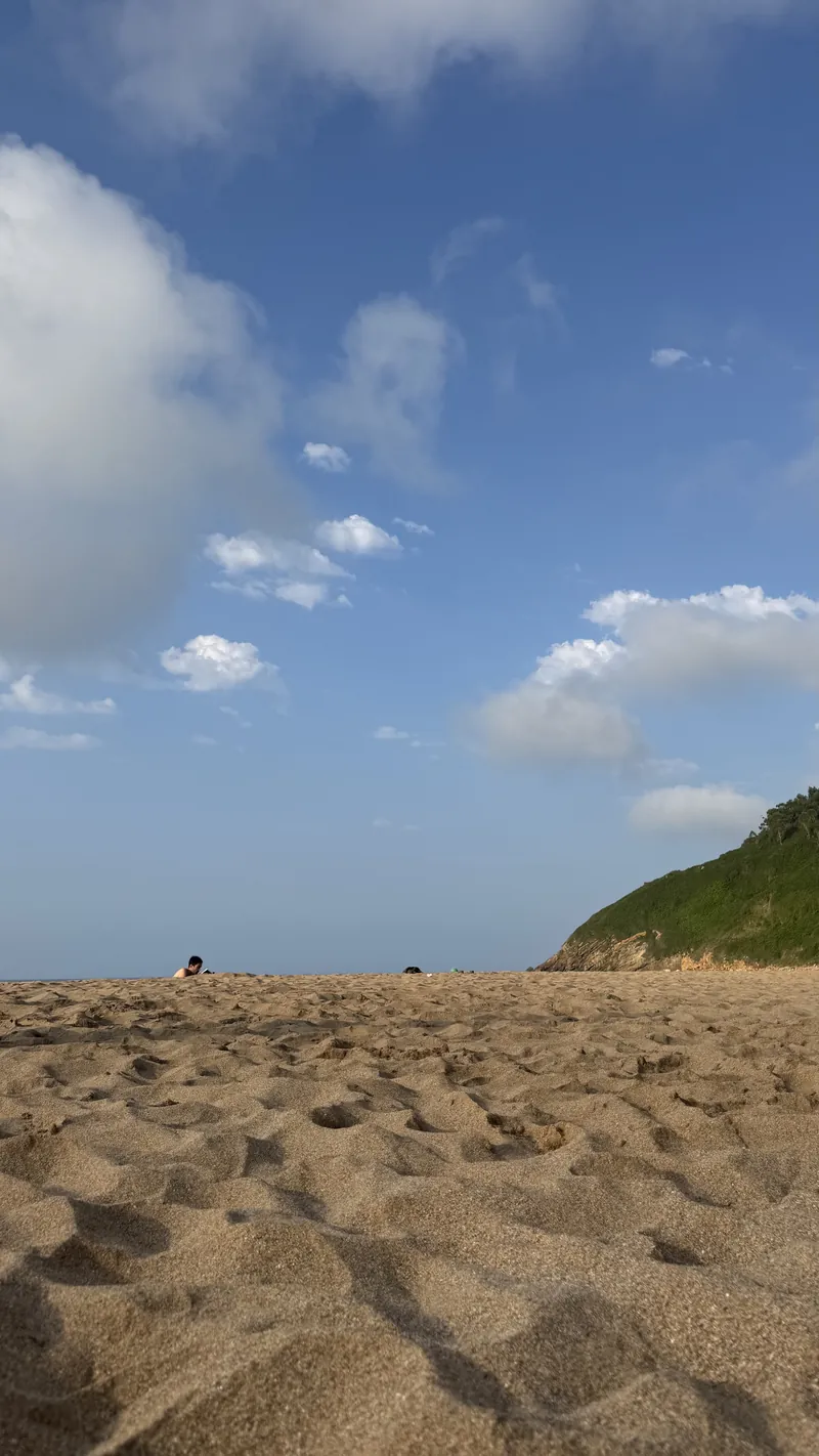 Der Sand des Arenal de Morís unter blauem Himmel, dahinter der grüne Hang