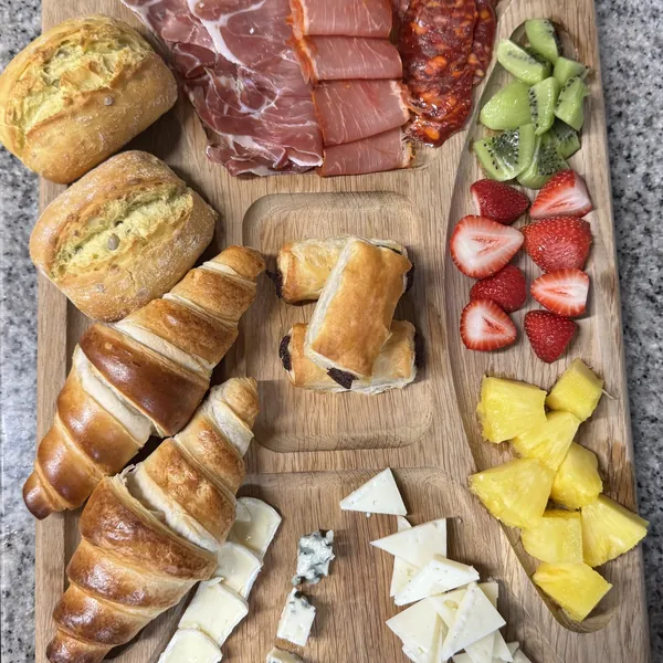 Breakfast board with bread, croissants, ham, chorizo, cheeses and fruit
